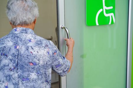 Asian senior elderly old lady woman patient open toilet bathroom by hand in nursing hospital ward : healthy strong medical concept.の写真素材