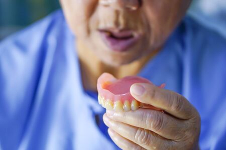 Asian senior or elderly old woman patient holding to use denture in nursing hospital ward : healthy...
