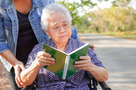 Asian senior or elderly old lady woman patient reading a book while sitting on wheelchair in park : healthy strong medical concept の写真素材