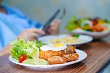 Asian senior or elderly old lady woman patient eating breakfast vegetable healthy food with hope and happy while sitting and hungry on bed in hospital.の写真素材