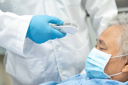 Doctor holding digital thermometer to measures asian senior or elderly old lady woman patient wearing a face mask have a fever in hospital : healthy strong medical concept.の写真素材