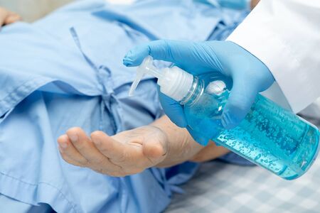 Doctor holding and press blue alcohol sanitizer gel for senior woman patient to protect infection and kill Novel Coronavirus (2019-nCoV) Covid-19 virus, bacteria and germs.の写真素材