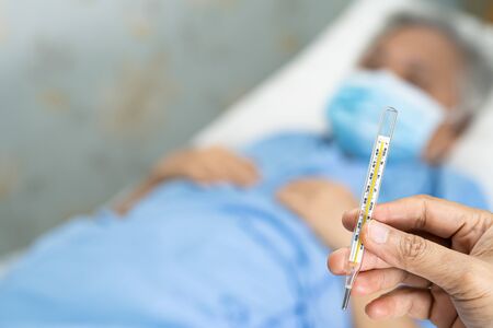 Doctor holding thermometer to measures asian senior or elderly old lady woman patient wearing a face...