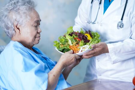 Asian senior or elderly old lady woman patient eating breakfast vegetable healthy food with hope and happy while sitting and hungry on bed in hospital.の写真素材