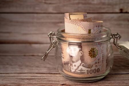 Thai baht banknotes in grass jar on wooden background, business saving finance investment concept.
