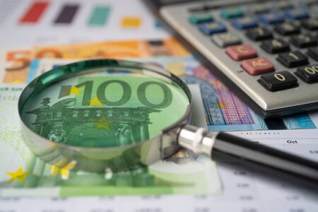 Eyeglass with calculator on Euro banknotes and graph paper background.