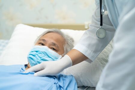Doctor using stethoscope to checking Asian senior or elderly old lady woman patient wearing a face mask in hospital for protect infection and kill Novel Coronavirus Covid-19 virus.の写真素材