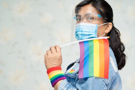 Asian lady wearing blue jean jacket or denim shirt and holding rainbow color flag, symbol of LGBT pride month celebrate annual in June social of gay, lesbian, bisexual, transgender, human rights.の写真素材