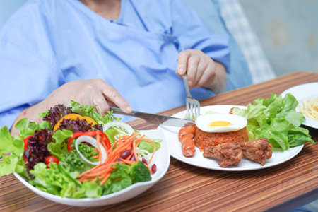 Asian senior or elderly old lady woman patient eating breakfast vegetable healthy food with hope and happy while sitting and hungry on bed in hospital.の写真素材
