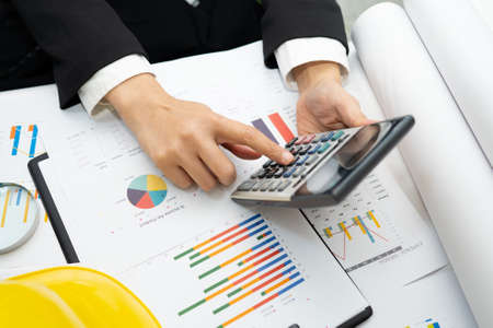 Architect or engineer working project accounting with graph and construction helmet in office,...