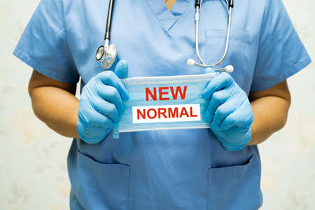 Doctor holding mask with New normal text after COVID-19 coronavirus pandemic.