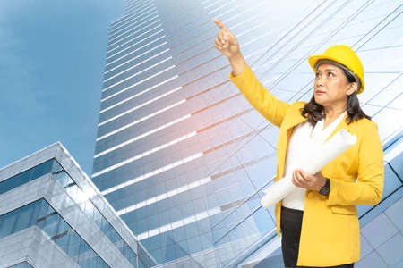 Asian engineer woman with blueprint standing at building background with copy space, engineering construction and architecture concept.の写真素材