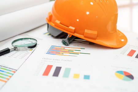 Yellow construction helmet with blueprint on graph, engineer safety concept.の写真素材