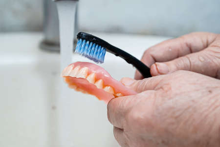 Asian senior or elderly old woman patient use toothbrush to clean partial denture of replacement teeth.の写真素材