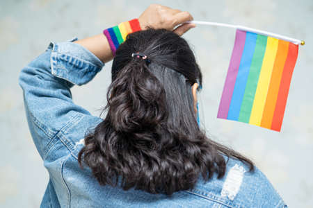Asian lady wearing mask and face shield for protect covid-19 virus holding rainbow flag, symbol of LGBT pride month celebrate annual in June social of gay, lesbian, bisexual, transgender, human rights.の写真素材