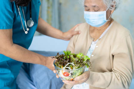 Asian senior or elderly old lady woman patient eating breakfast vegetable healthy food with hope and happy while sitting and hungry on bed in hospital.の写真素材