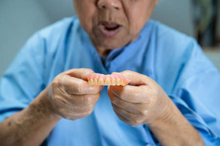 Asian senior or elderly old woman patient holding to use denture in nursing hospital ward, healthy strong medical conceptの写真素材