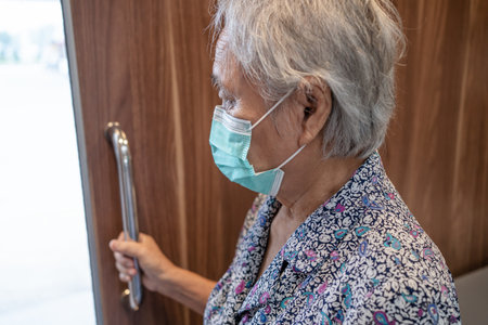 Asian senior or elderly old lady woman patient wearing face mask use toilet bathroom handle security in nursing hospital ward, healthy strong medical concept.の写真素材