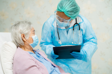 Asian doctor wearing face shield and PPE suit new normal to check patient protect safety infection Covid-19 Coronavirus outbreak at quarantine nursing hospital ward.の写真素材