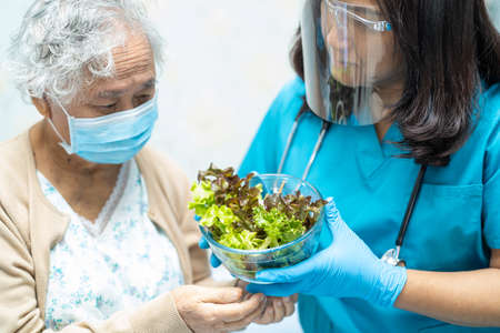 Asian senior or elderly old lady woman patient eating breakfast vegetable healthy food with hope and happy while sitting and hungry on bed in hospital.の写真素材