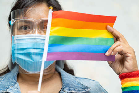 Asian lady wearing blue jean jacket or denim shirt and holding rainbow color flag, symbol of LGBT...