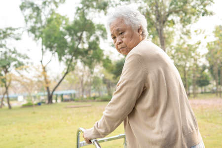 Asian senior or elderly old lady woman patient walk with walker in park with copy space, healthy strong medical conceptの写真素材