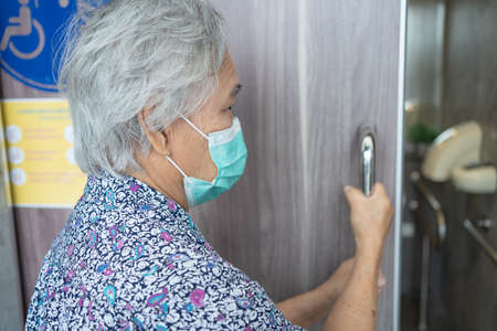 Asian senior woman patient wearing a face mask open the toilet door for protect Covid 19  virus.の写真素材