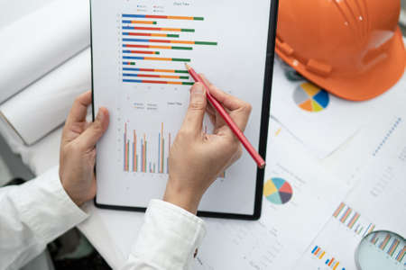 Engineer working project accounting with graph and construction helmet in office, Construction...