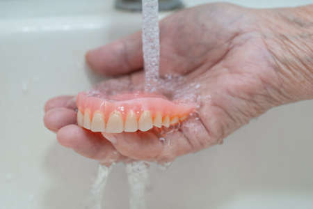 Asian senior or elderly old woman patient holding partial denture of replacement teeth.の写真素材