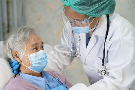 Doctor holding hands Asian senior or elderly old lady woman infected patient with love, care, helping, encourage and empathy in quarantine room   outbreak at nursing hospital ward.の写真素材