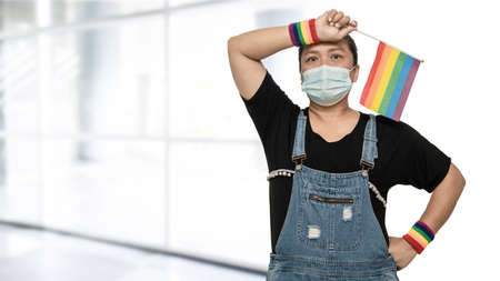 Asian lady wearing mask for protect covid-19 virus holding rainbow flag, symbol of LGBT pride month celebrate annual in June social of gay, lesbian, bisexual, transgender, human rights.の写真素材