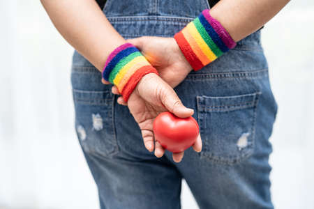 Asian lady wearing rainbow flag wristbands and hold red heart, symbol of LGBT pride month celebrate annual in June social of gay, lesbian, bisexual, transgender, human rights.の写真素材