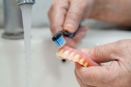 Asian senior or elderly old woman patient use toothbrush to clean partial denture of replacement teeth.の写真素材