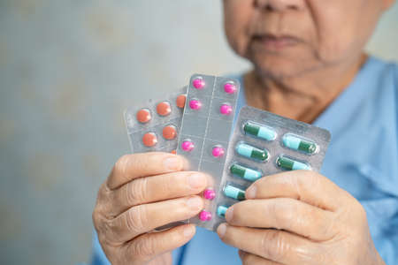 Asian senior or elderly old lady woman patient holding antibiotics capsule pills in blister...