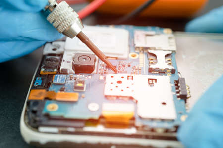Technician repairing inside of mobile phone by soldering iron. Integrated Circuit. the concept of...