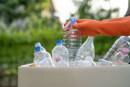 Asian woman volunteer carry water plastic bottles into garbage box trash in park, recycle waste...