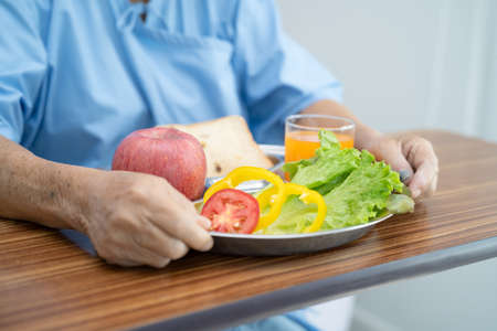 Asian senior or elderly old lady woman patient eating breakfast vegetable healthy food with hope and happy while sitting and hungry on bed in hospital.の写真素材