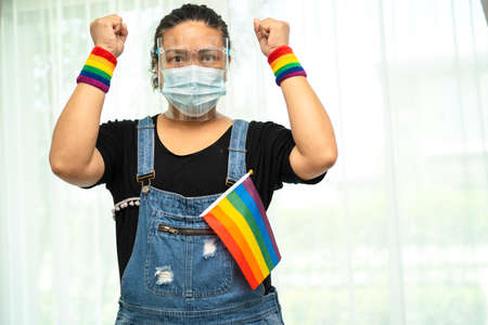Asian lady wearing blue jean jacket or denim shirt and holding rainbow color flag, symbol of LGBT...