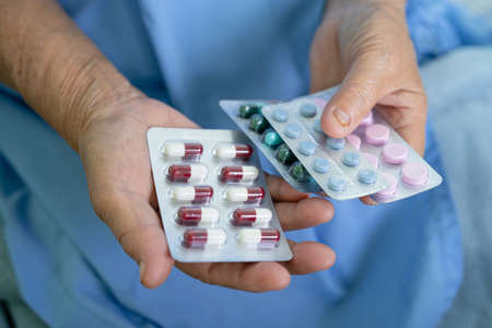 Asian senior or elderly old lady woman patient holding antibiotics capsule pills in blister...