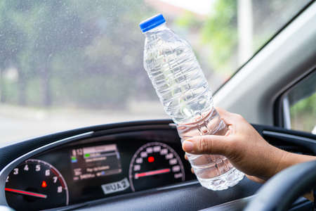 Asian woman driver holding bottle for drink water while driving a car. Plastic hot water bottle...