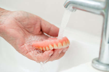 Asian senior or elderly old woman patient holding and washing denture in nursing hospital ward; healthy strong medical conceptの写真素材