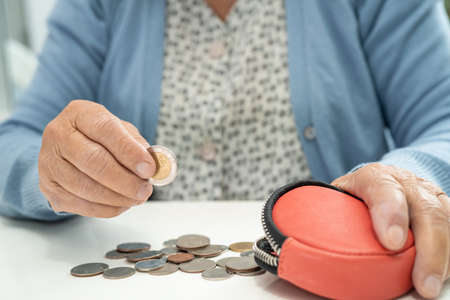 Asian senior or elderly old lady woman holding counting coin money in purse. Poverty, saving problem...