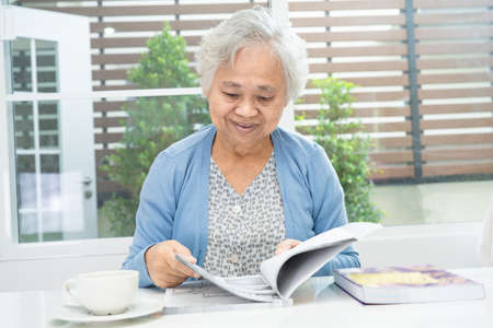 Asian senior or elderly old lady woman reading a book for practice brain while living at home,...