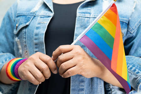Asian lady wearing blue jean jacket or denim shirt and holding rainbow color flag, symbol of LGBT...