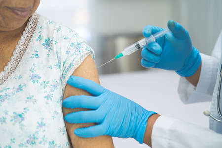 Elderly Asian senior woman wearing face mask getting covid-19 or coronavirus vaccine by doctor make injection.の写真素材