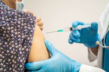 Elderly Asian senior woman wearing face mask getting vaccine by doctor make injection.の写真素材