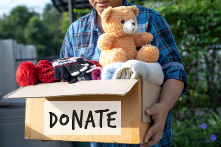 Holding clothing donation box with used clothes and doll at home to support help for poor people in the world.の写真素材