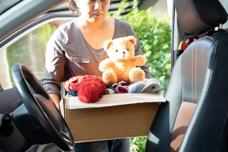 Volunteer woman provide clothing donation box with used clothes and doll in car to support help for refugee, homeless or poor people in the world.の写真素材