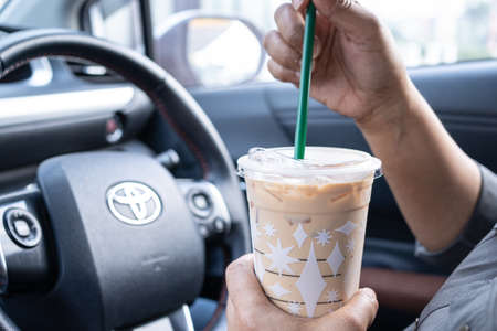 Bangkok, Thailand - December 1, 2021 Asian lady holding ice coffee in car dangerous and risk an accident.のeditorial素材