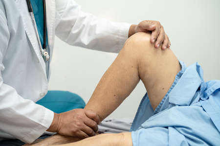 Asian doctor physiotherapist examining, massaging and treatment knee and leg of senior patient in orthopedist medical clinic nurse hospital.の写真素材